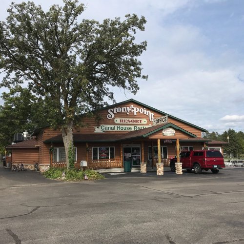 A rustic building with a sign reading "Stony Point Resort" surrounded by trees and parked cars.