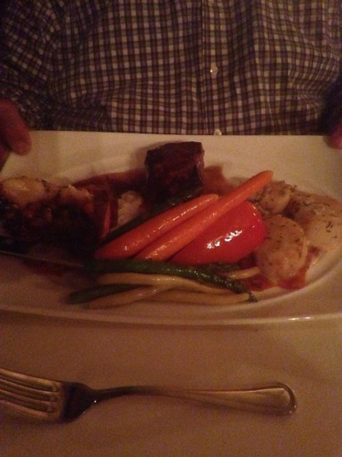 A plate of grilled meat and vegetables, including carrots, bell peppers, and asparagus, served on a white dish.