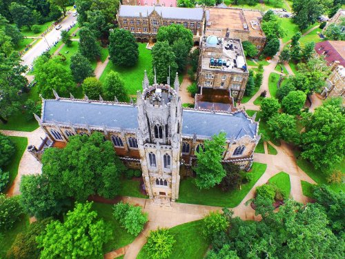 Aerial view of a historic stone building surrounded by lush green trees and pathways on a university campus.