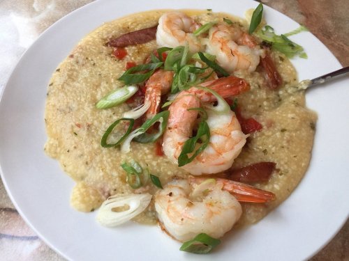 A plate of shrimp and grits topped with green onions and diced tomatoes, served in a creamy sauce.
