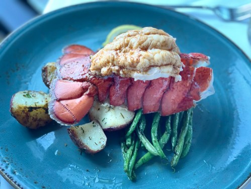 A gourmet dish featuring lobster tail on a bed of green beans and roasted potatoes, garnished with lemon.