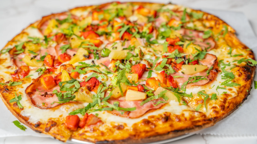 A delicious pizza topped with ham, pineapple, red peppers, and fresh herbs on a golden crust.