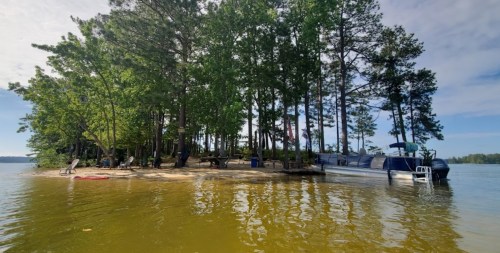 A serene lakeside scene featuring a small island with trees and a boat docked nearby, reflecting in the calm water.