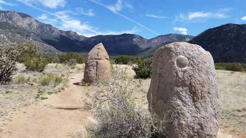 Two large stone monoliths stand in a grassy area, with mountains and blue sky in the background.