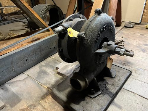 An old, rusted mechanical pump sits on a wooden floor, surrounded by tools and machinery.