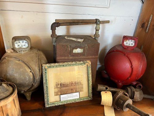 Vintage industrial equipment displayed on a wooden shelf, including tanks, a pump, and an old photograph.