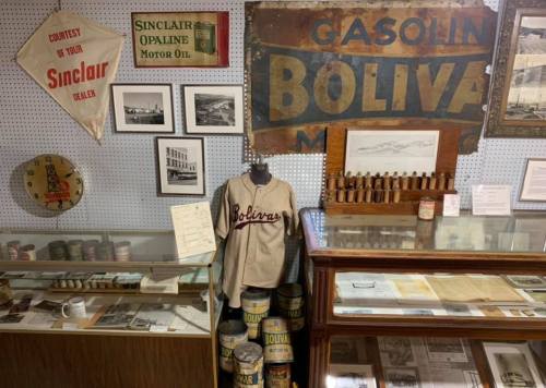 A display featuring vintage signs, photographs, and memorabilia, including a Bolivar baseball jersey and oil cans.