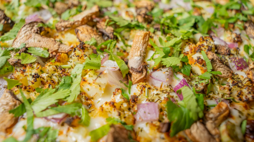 Close-up of a pizza topped with mushrooms, onions, and fresh herbs, showcasing a golden, cheesy crust.