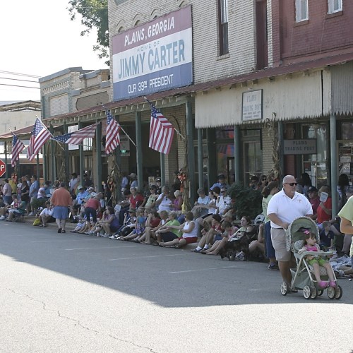 Crowd of people sitting along a street in Plains, Georgia, with American flags and a sign for Jimmy Carter.