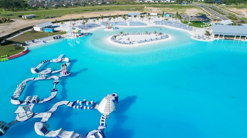 Aerial view of a large, blue water park with slides, loungers, and an island in the center.
