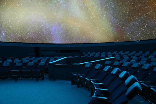 A dark planetarium with curved seating facing a starry sky projection on the dome ceiling.