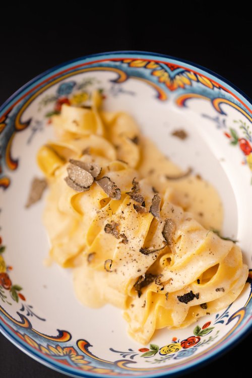 A bowl of creamy pasta topped with shaved truffles, served in a decorative dish.