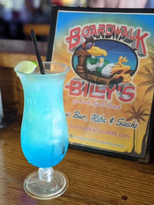 A vibrant blue cocktail with a lime slice, placed in front of a colorful menu for Boardwalk Billy's.