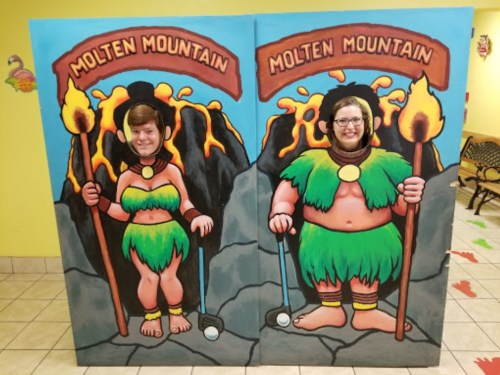 Two people pose in a colorful cutout board depicting characters from "Molten Mountain," surrounded by lava and rocks.