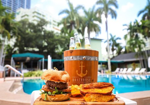 A delicious burger with plantain chips in front of a pool, with a bucket of drinks nearby and palm trees in the background.