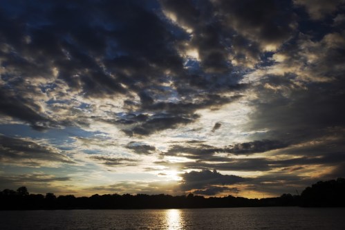 Sunset over a calm lake, with dramatic clouds reflecting warm hues in the sky.
