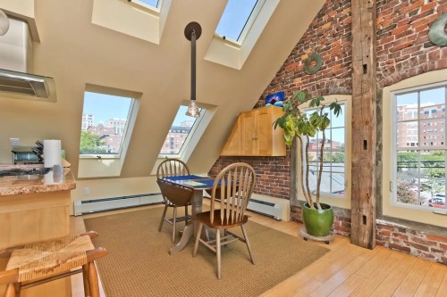 Cozy dining area with a wooden table, chairs, and large windows showcasing a city view in a stylish loft.