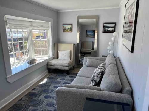 Cozy living room with a gray sofa, armchair, large window, and decorative artwork on the walls.