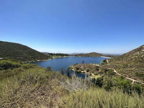 A serene lake surrounded by hills and greenery under a clear blue sky.