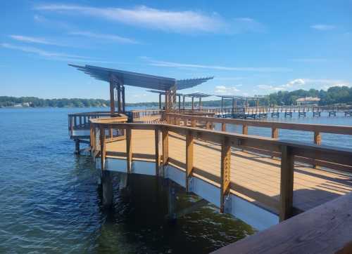 A wooden dock extends over calm water, featuring a shaded seating area and blue skies in the background.