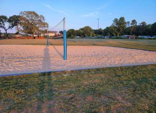 A sandy volleyball court at sunset, with a net and trees in the background.