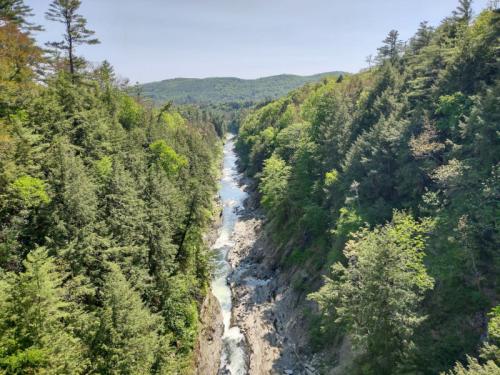 A scenic view of a river winding through lush green forests and hills under a clear blue sky.
