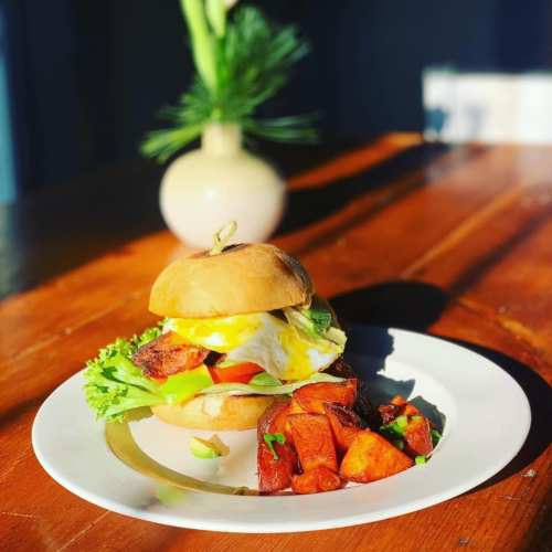 A delicious burger with lettuce, tomato, and an egg, served with seasoned potato wedges on a wooden table.