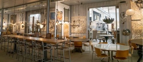 A stylish interior featuring various art pieces, chandeliers, and a mix of dining tables and chairs.