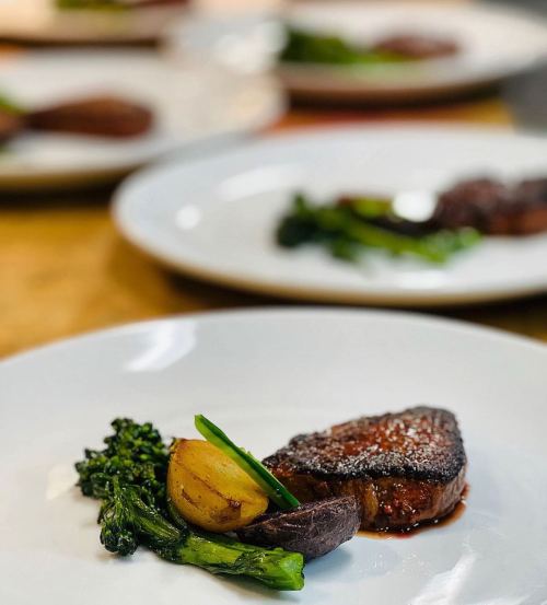 A plated dish featuring seared meat, roasted potatoes, and sautéed greens on a white plate.