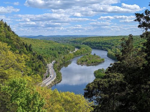 A scenic view of a winding river surrounded by lush green trees and a blue sky with fluffy clouds.