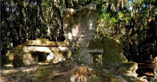 Ruins of a stone structure surrounded by lush greenery and trees, with moss hanging from branches.