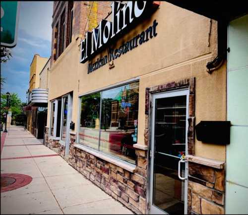 Exterior view of El Molino Mexican Restaurant, featuring a stone facade and large windows along a city sidewalk.