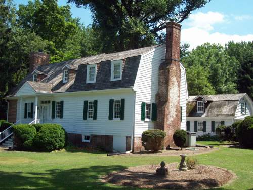 A charming white house with green shutters, surrounded by lush trees and a well-maintained lawn.