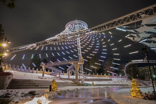 A brightly lit amusement park ride surrounded by snow, with colorful lights illuminating the night sky.