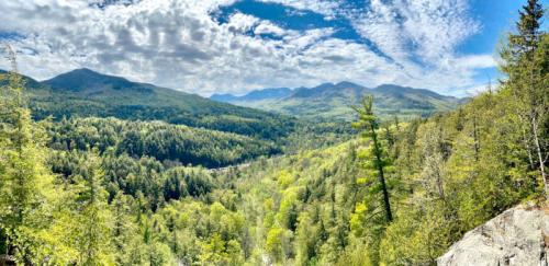 A panoramic view of lush green mountains under a partly cloudy sky, showcasing a vibrant valley below.