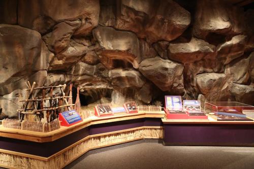 A museum exhibit featuring a rocky backdrop with displays of artifacts and information panels on wooden stands.
