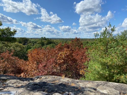A scenic view from a rocky outcrop, showcasing vibrant autumn foliage and a blue sky with fluffy clouds.