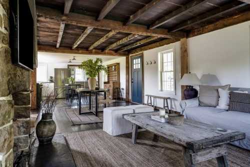 Cozy living room with wooden beams, a sofa, rustic coffee table, and a dining area in a bright, inviting space.