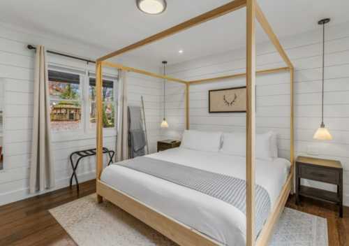 A modern bedroom featuring a four-poster bed, wooden accents, and large windows with natural light.