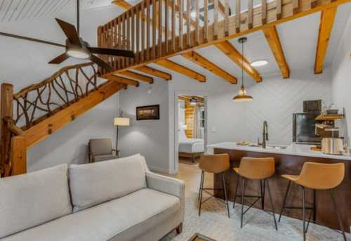 Cozy interior of a modern cabin featuring a living area, kitchen island, and wooden staircase leading to a loft.