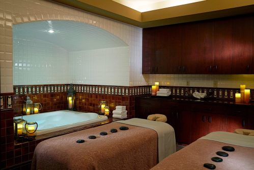 A serene spa room featuring a hot tub, massage tables, and soft lighting with candles and towels arranged neatly.