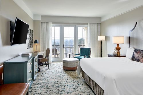 A modern hotel room featuring a king bed, TV, seating area, and balcony with scenic views.