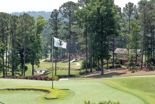 A golf course with a flag on the green, surrounded by trees and a scenic landscape in the background.