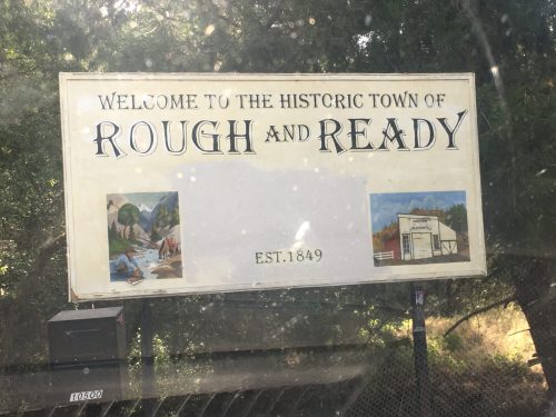 Sign welcoming visitors to the historic town of Rough and Ready, established in 1849, with scenic illustrations.