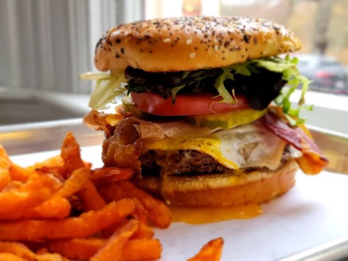 A juicy burger with lettuce, tomato, pickles, and bacon, served with a side of crispy sweet potato fries.