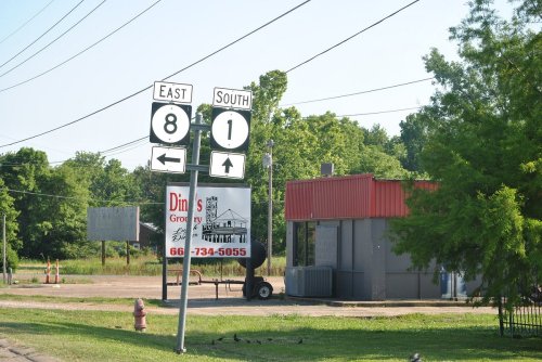 Road signs indicating East 8 and South 1 directions, with a small grocery store in the background.