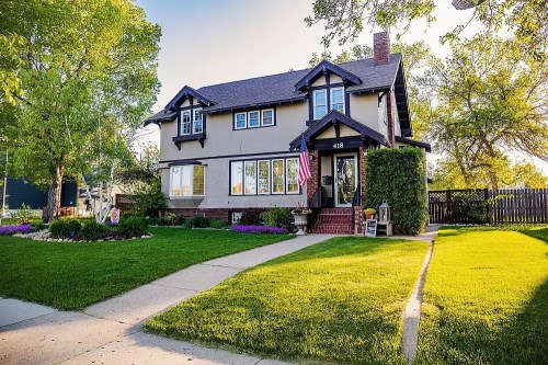 A charming two-story house with a front yard, American flag, and landscaped garden under a clear blue sky.