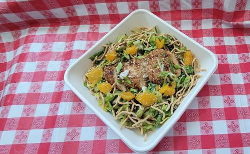 A bowl of salad with grilled chicken, mandarin oranges, and crunchy noodles on a red and white checkered tablecloth.