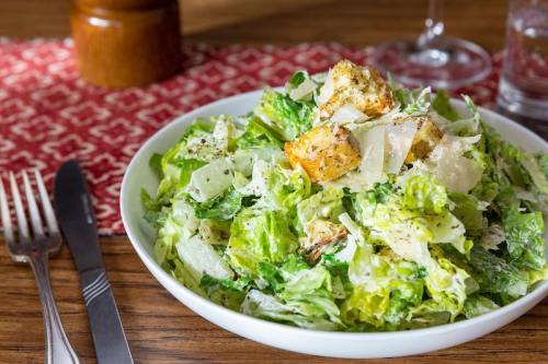 A fresh Caesar salad with romaine lettuce, croutons, and grated Parmesan cheese in a white bowl on a wooden table.