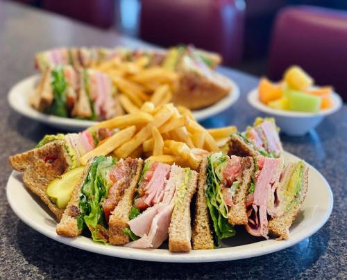 A plate of sandwiches with layers of meat, lettuce, and tomato, served with fries and a side of fruit.